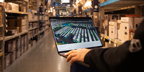 Lowe's Innovation Labs team member on a laptop in a Lowe's Home Improvement store aisle reviewing the store's digital twin. 