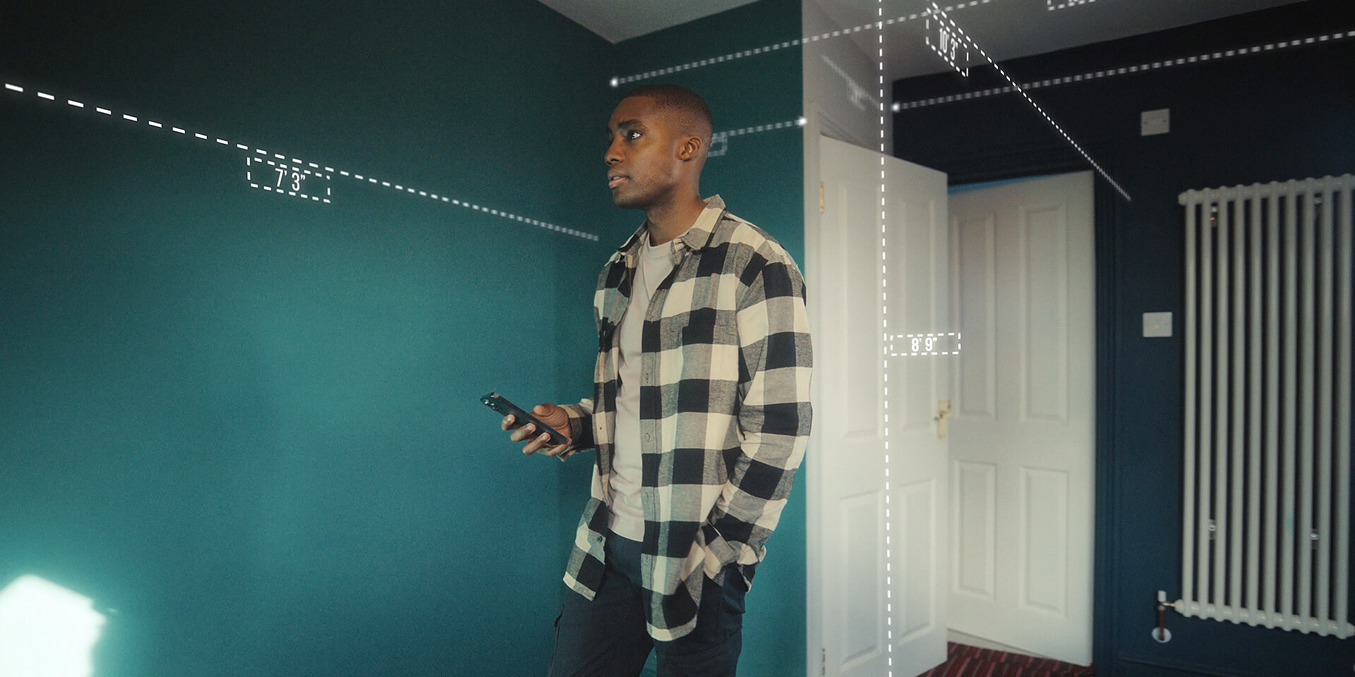 Male in home measuring his room's dimensions with his mobile device. 