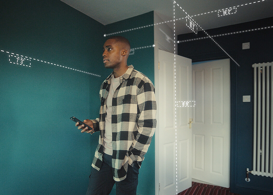 Male in home measuring his room's dimensions with his mobile device. 