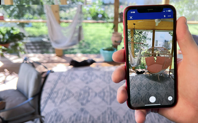 Person holding mobile phone looking at a virtual product in their outside living area through Lowe's Home Improvement AR visualizer. 