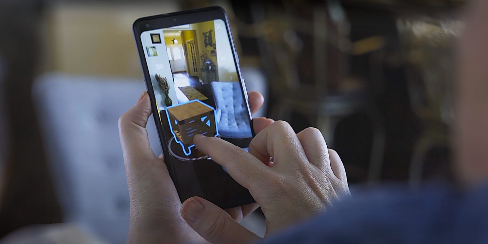 Person holding mobile phone looking at a virtual end table in their living room Lowe's Home Improvement AR visualizer. 