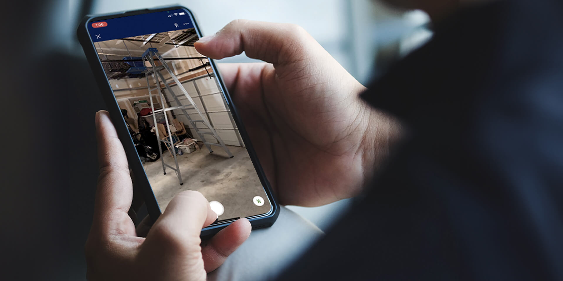 Person holding mobile phone looking at a virtual ladder in their garage through Lowe's Home Improvement AR visualizer. 