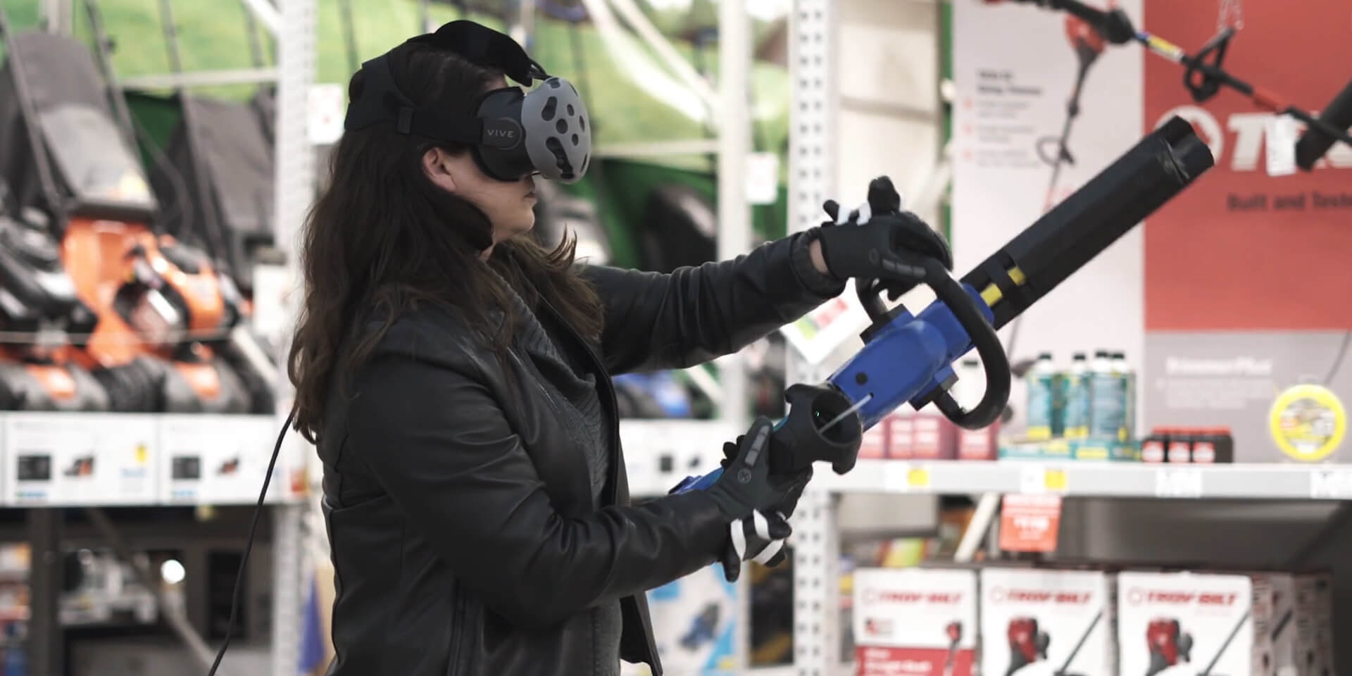 Female customer holding a powertool-shaped controller learning how to trim hedges in a VR environment. 